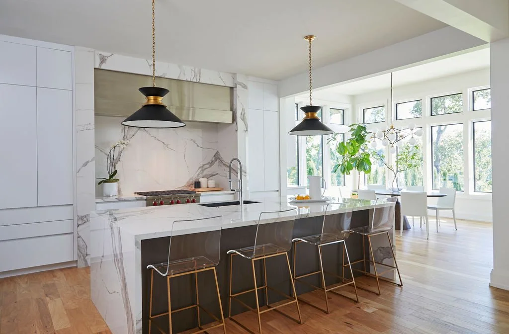Modern white kitchen with dramatic full-height stone backsplash, waterfall island and black pendant lights