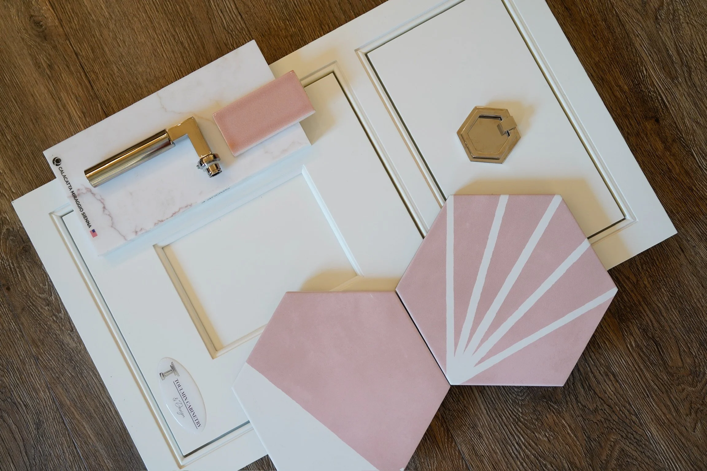 Flat lay of bathroom design selections including cabinetry door styles, brass hardware, marble-look surfaces, and pink tile samples by Toulmin Kitchen & Bath in Tuscaloosa, Alabama.