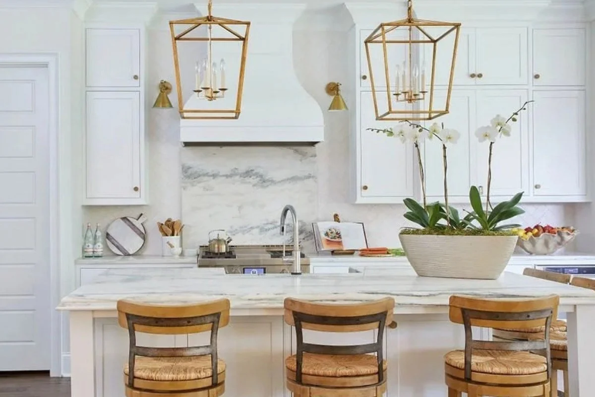 White kitchen with dramatic stone slab backsplash behind the range, brass lantern pendants and wood counter stools