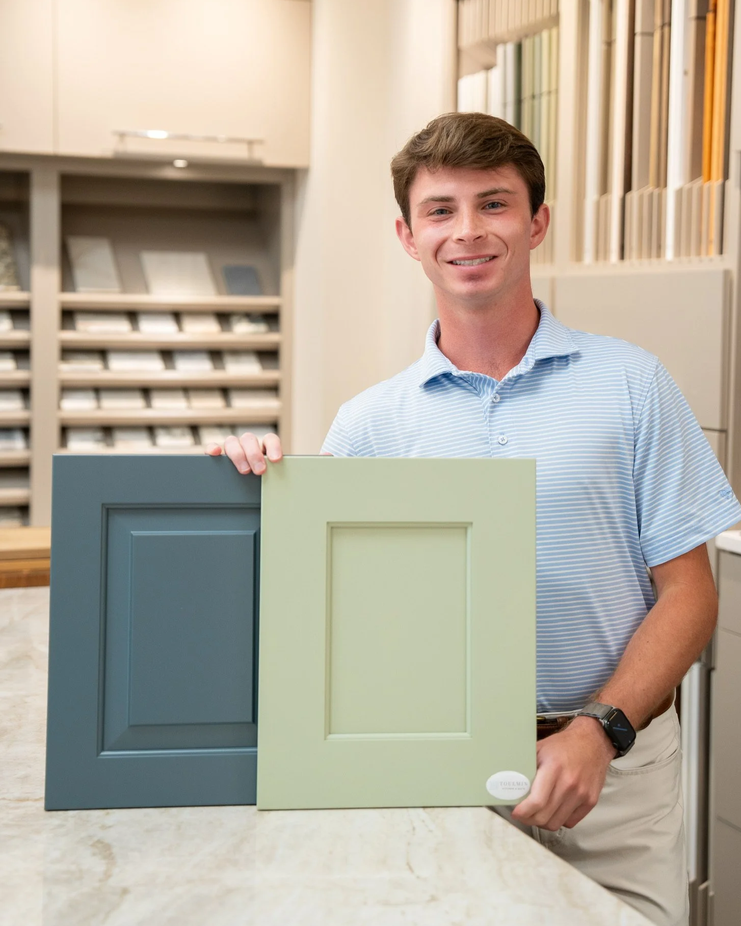 Kitchen designer at Toulmin Kitchen & Bath holding blue and green cabinet door samples inside a luxury cabinetry showroom in Tuscaloosa, Alabama.