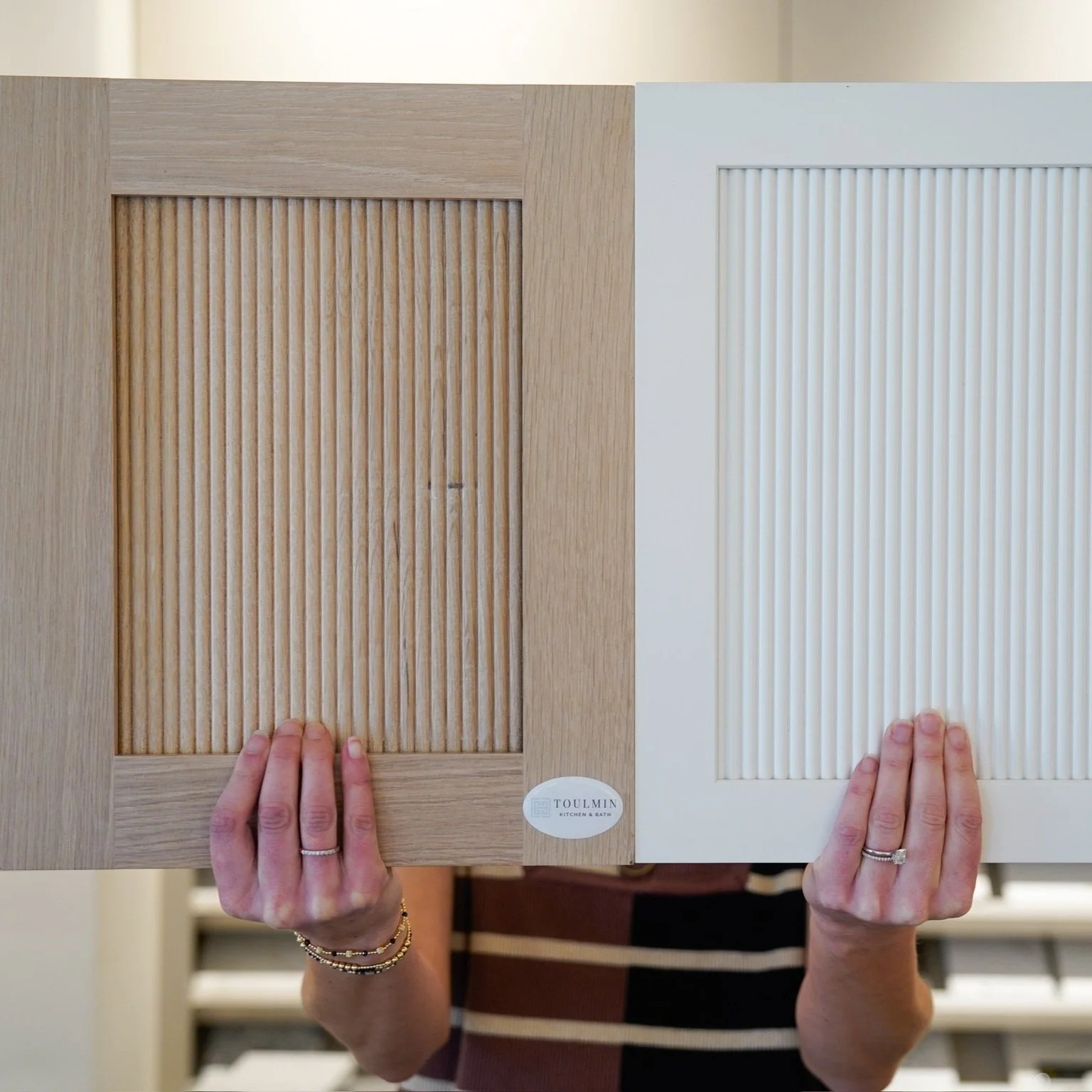 Close-up of two reeded cabinet door samples, one in natural white oak and one painted white, showcasing the textured vertical fluting detail popular in luxury kitchen and bathroom cabinetry design.