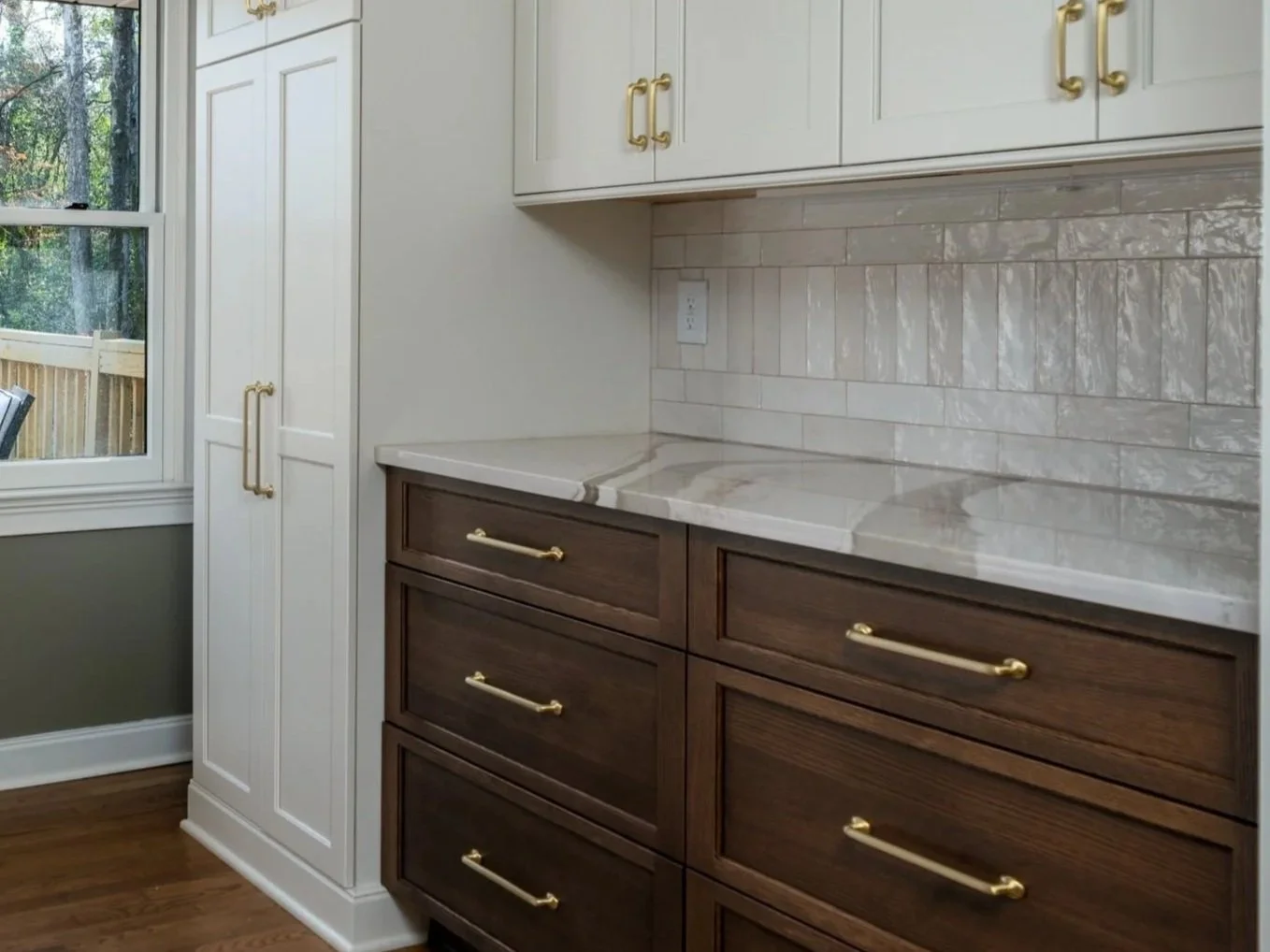 White upper cabinets and dark-stained wood drawers with brass hardware, a light stone countertop, and a glossy white tile backsplash.