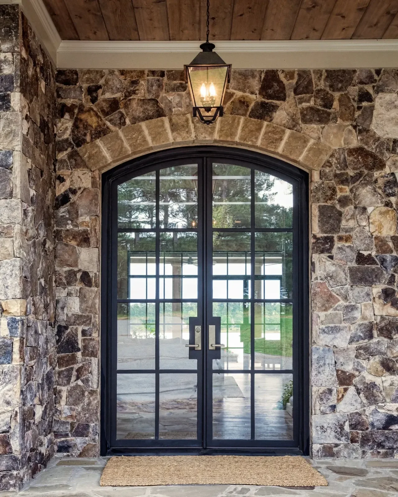 Custom black steel and glass front doors framed by a stone exterior archway, creating a dramatic and elegant home entrance.