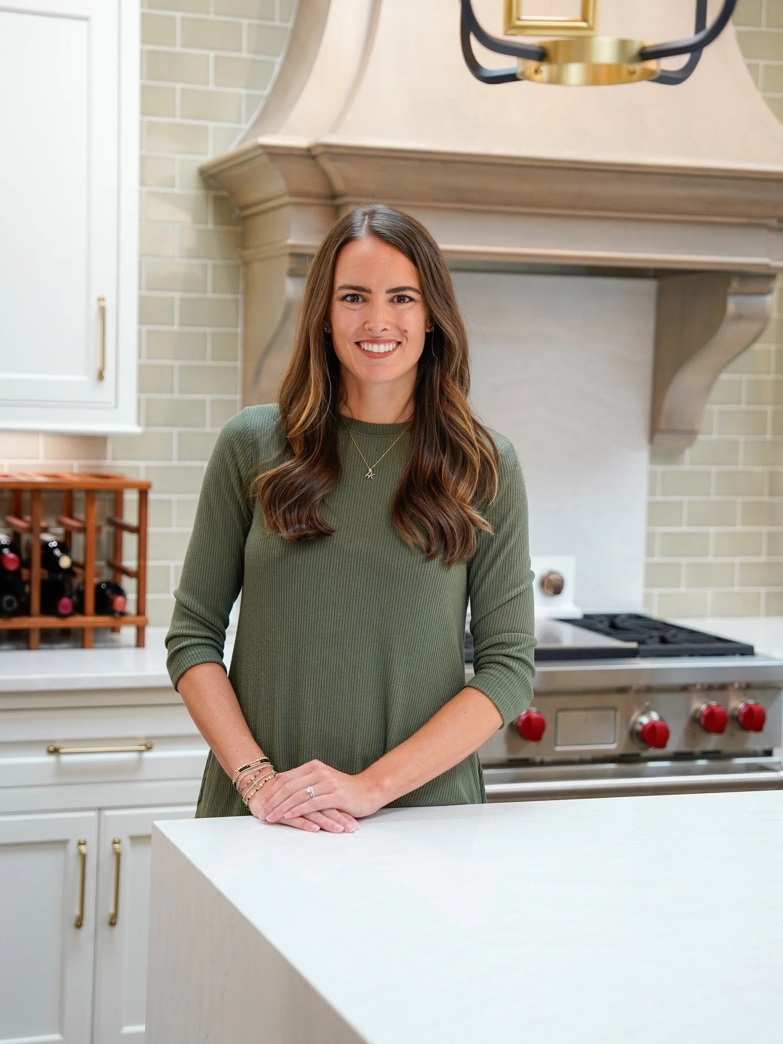 Kitchen designer standing behind a large island with a white quartz countertop featuring a clean eased edge, set in a bright kitchen with custom cabinetry and a statement range hood.