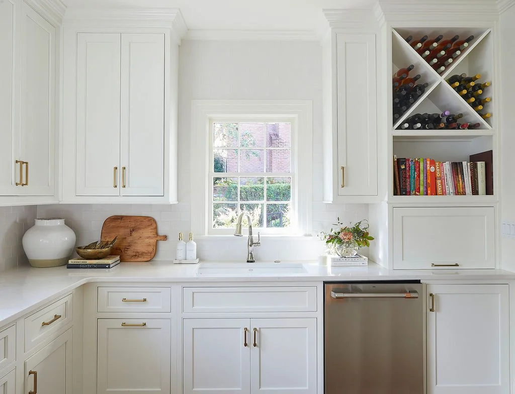 White kitchen cabinetry with brass hardware, sink storage, built-in dishwasher, and floor-to-ceiling wine storage.