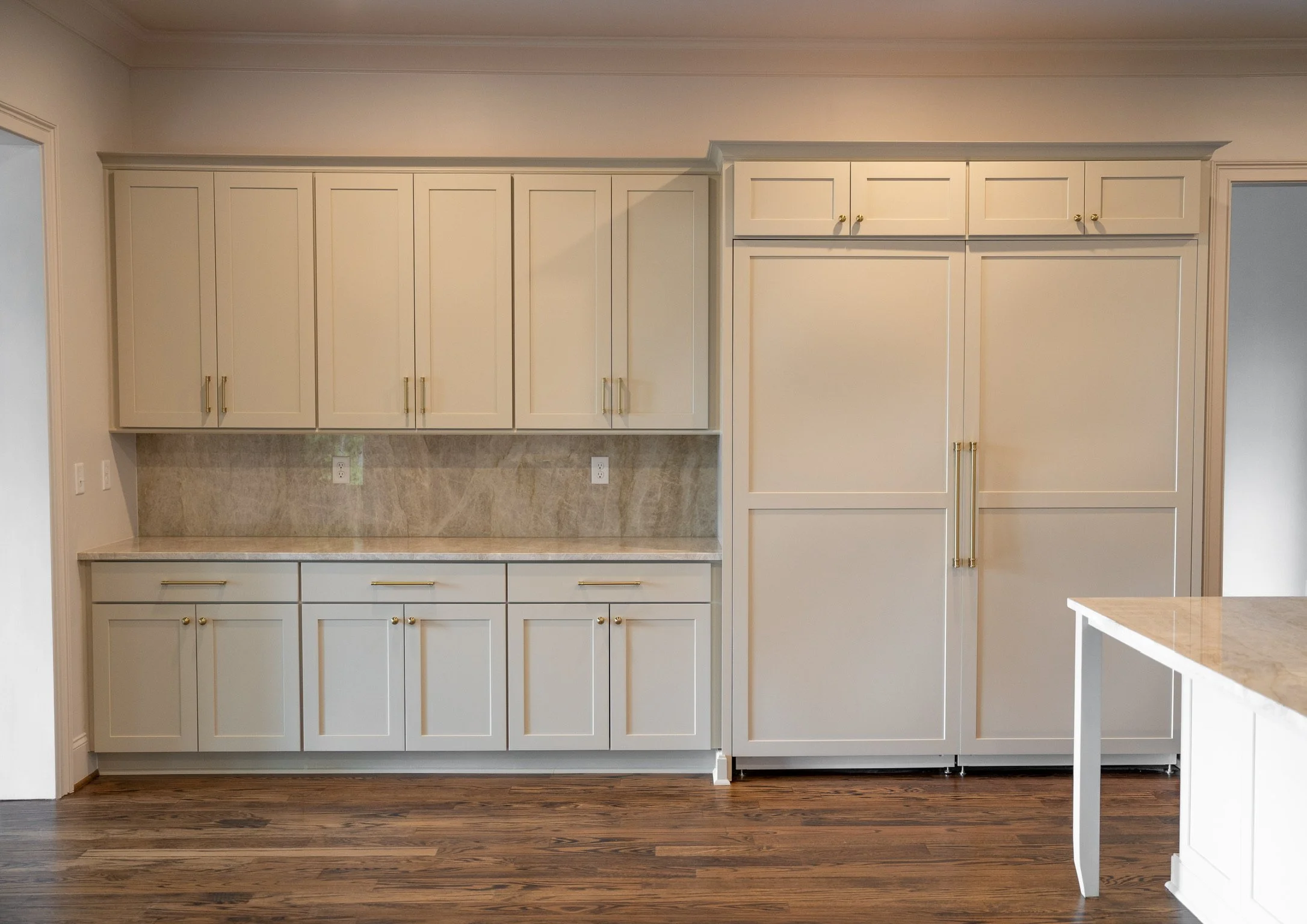 Custom white kitchen cabinetry with brass hardware, a built-in paneled refrigerator, stone backsplash and dark hardwood floors.