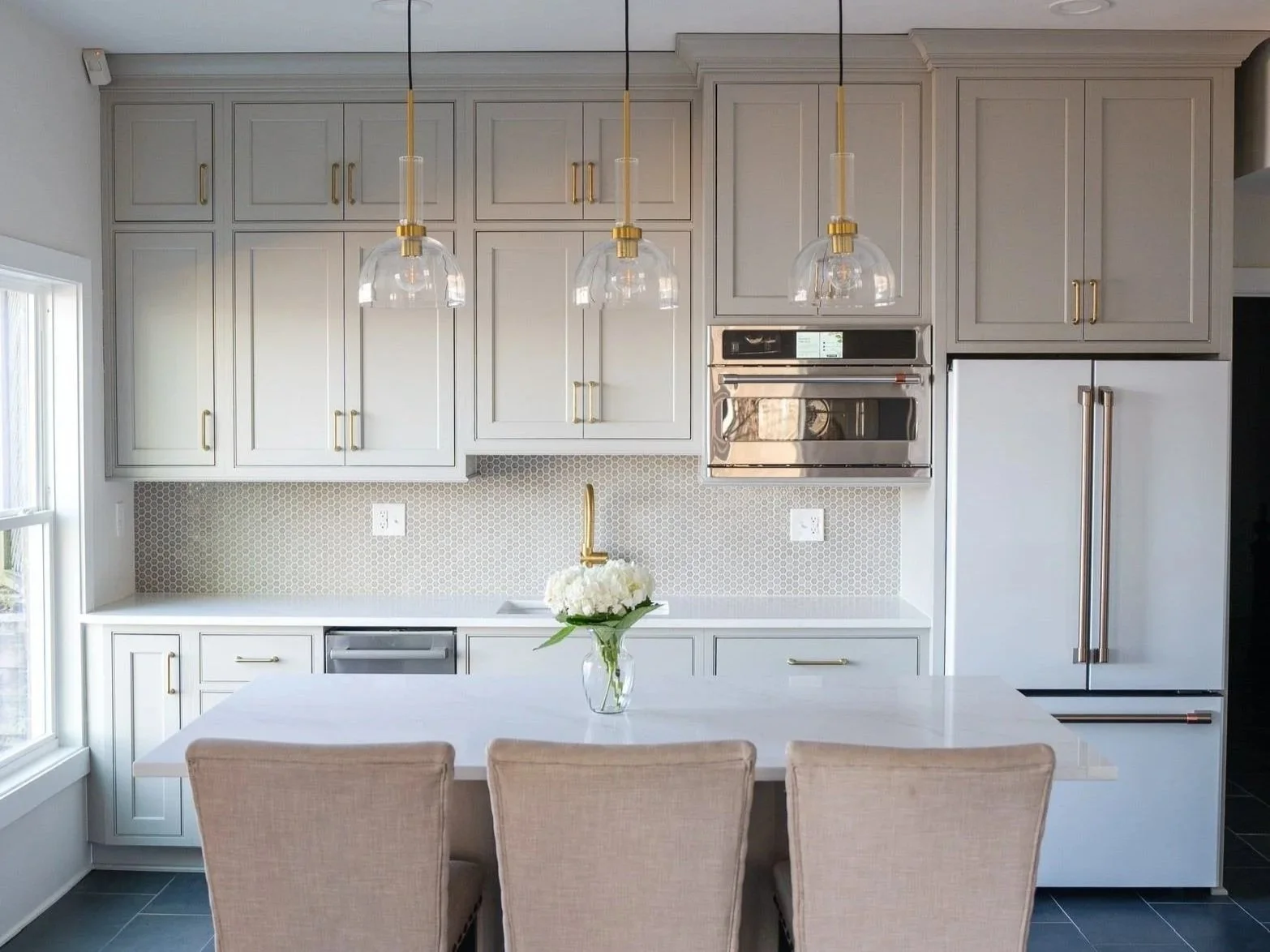 A kitchen featuring Shiloh cabinetry with brass hardware, glass pendant lighting, quartz countertops, and a light mosaic tile backsplash for a clean, timeless design