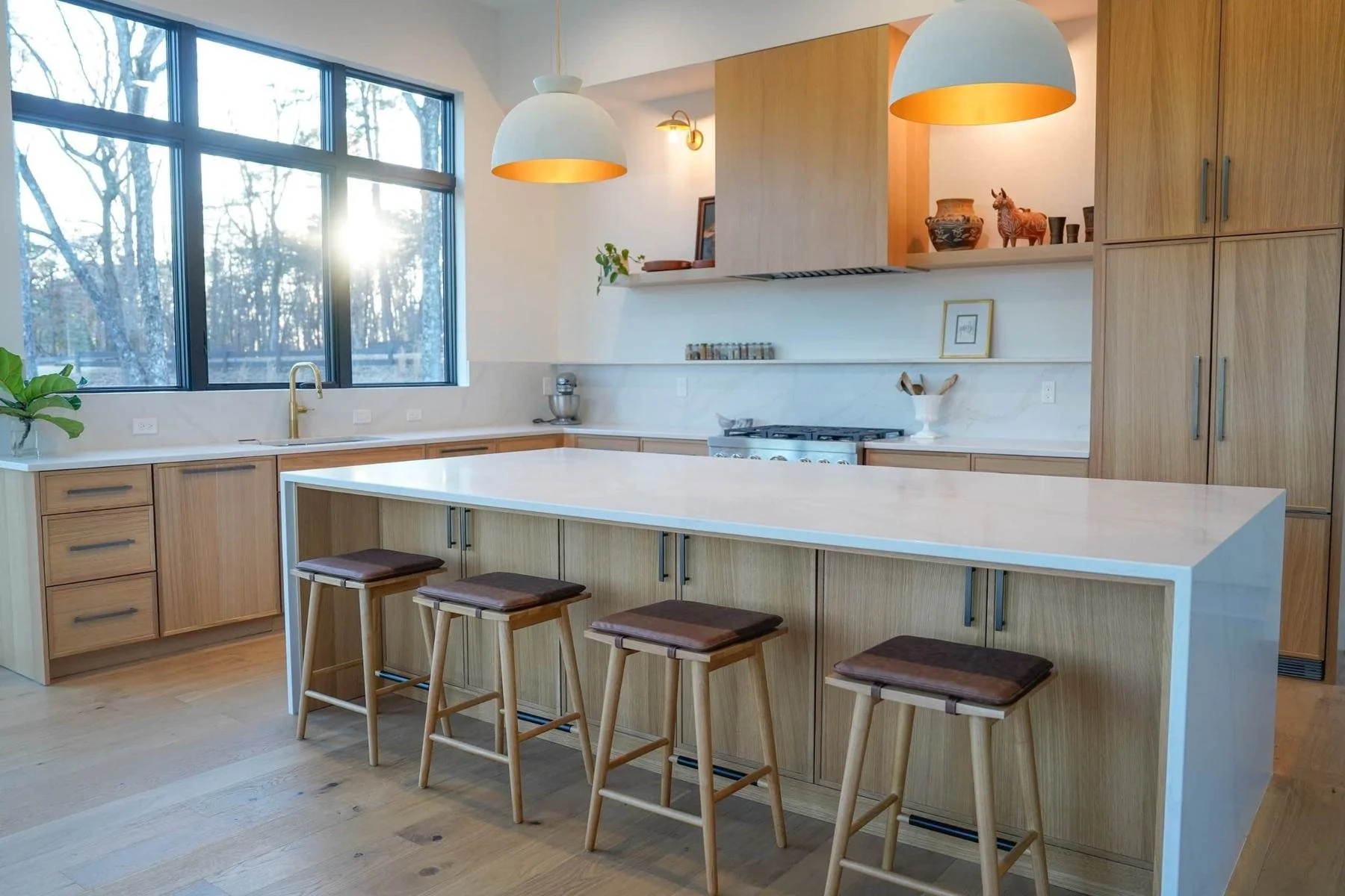 Modern kitchen with light wood flooring, natural wood cabinetry, a large island, and white countertops.