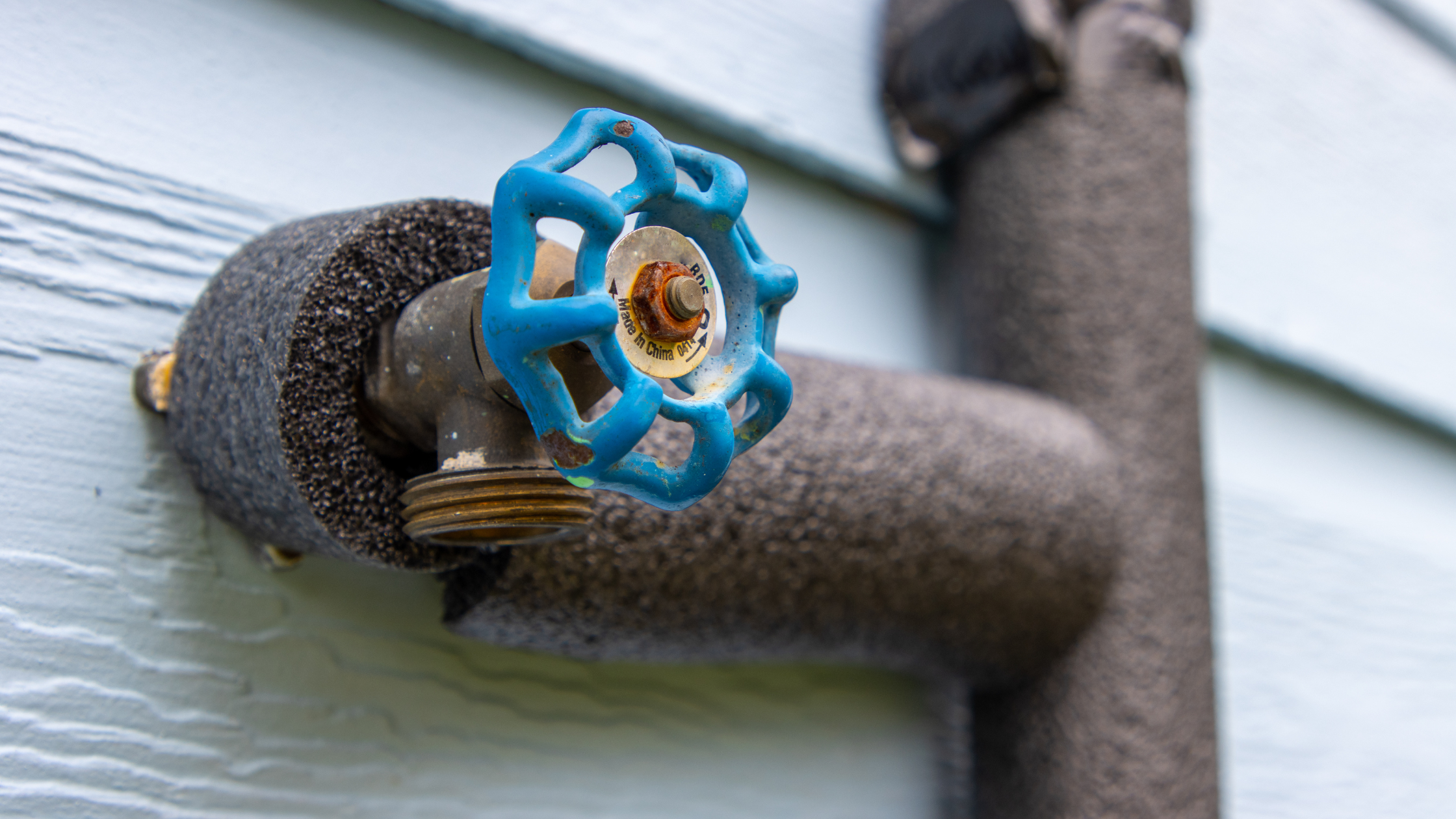 Close-up of an exterior water spigot with a blue handle, insulated with a foam cover to help protect outdoor plumbing from freezing temperatures.