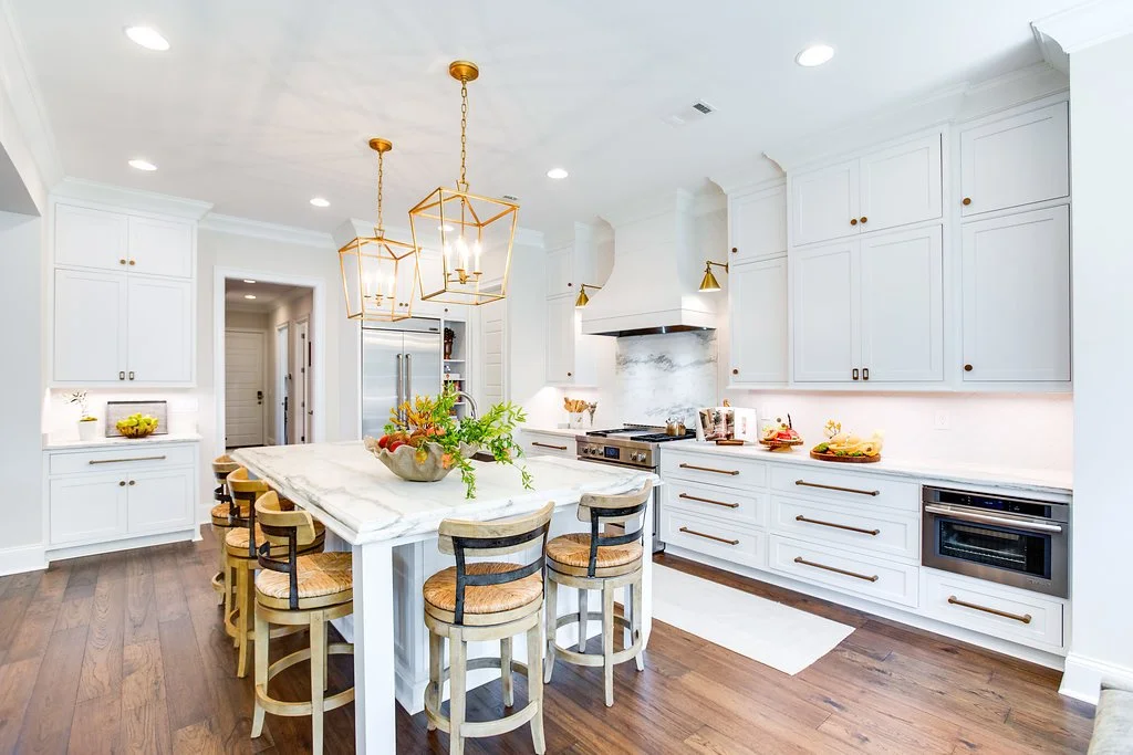 Engineered wood flooring in a bright kitchen with white cabinetry, a large marble island, and brass pendant lighting.