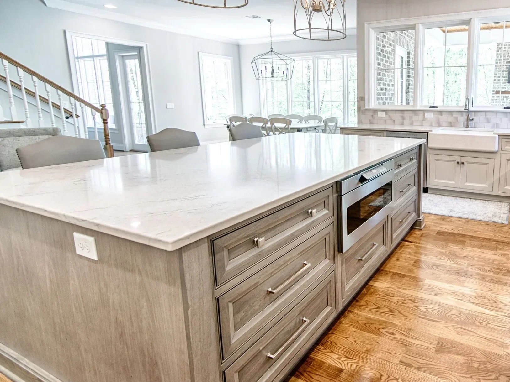 Bright, open-concept kitchen with a large island featuring a white quartz countertop with an eased edge, light wood cabinetry, built-in microwave, and views into a dining area with large windows.