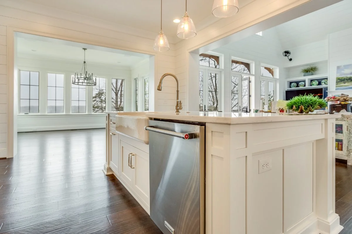 Bright open kitchen with a large custom island, farmhouse sink, wide walkways, pendant lighting, and an adjoining sunroom.