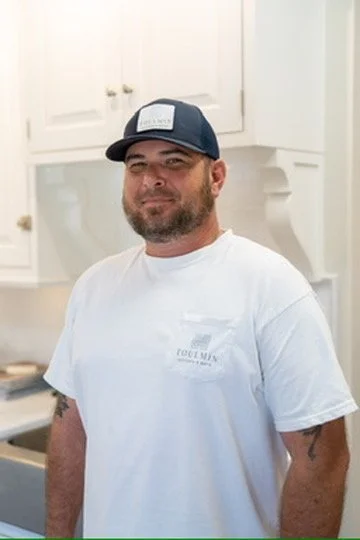 A man wearing a gray and white baseball cap and a navy blue polo shirt with the logo and text "TOULMIN Kitchen & Bath," standing against a light-colored background.
