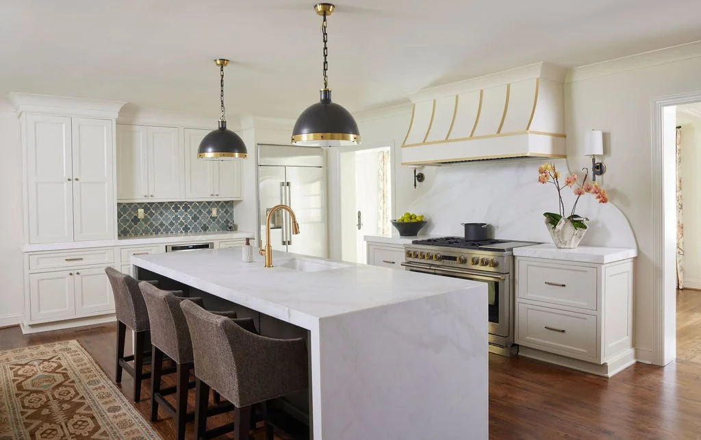Modern kitchen with a waterfall mitered edge island in white quartz, featuring integrated cabinetry, brass fixtures, upholstered bar stools, and a custom range wall.