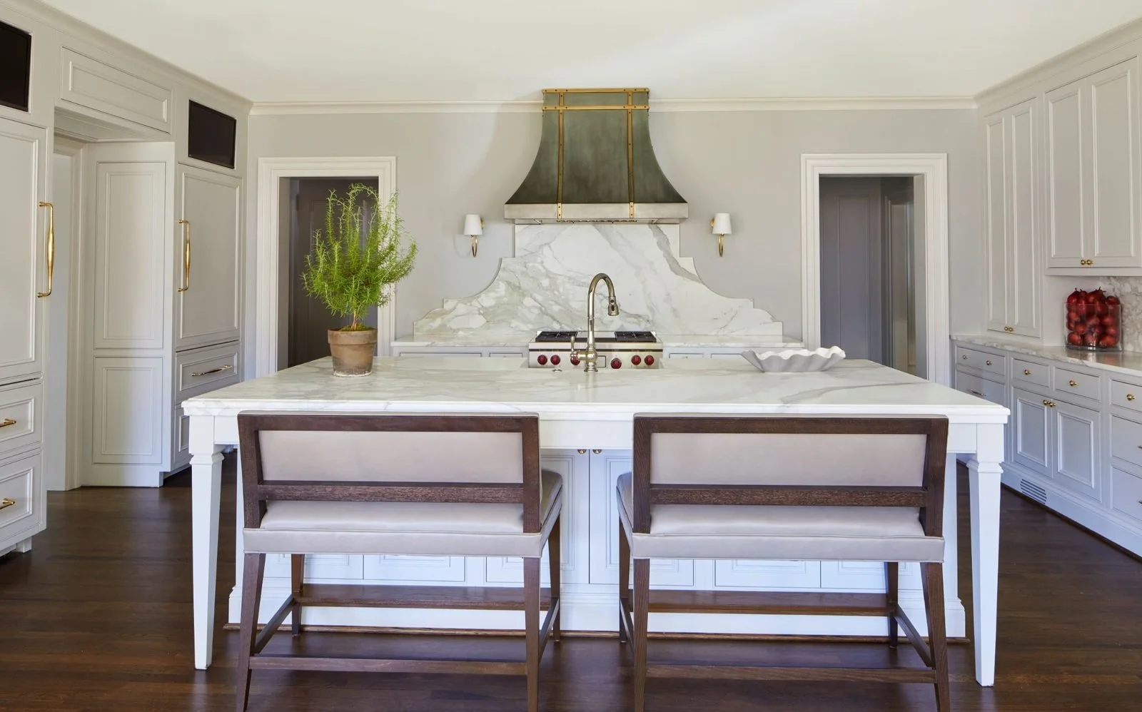 Traditional white kitchen with a marble-topped island, brass-accented range hood, and floor-to-ceiling cabinetry.