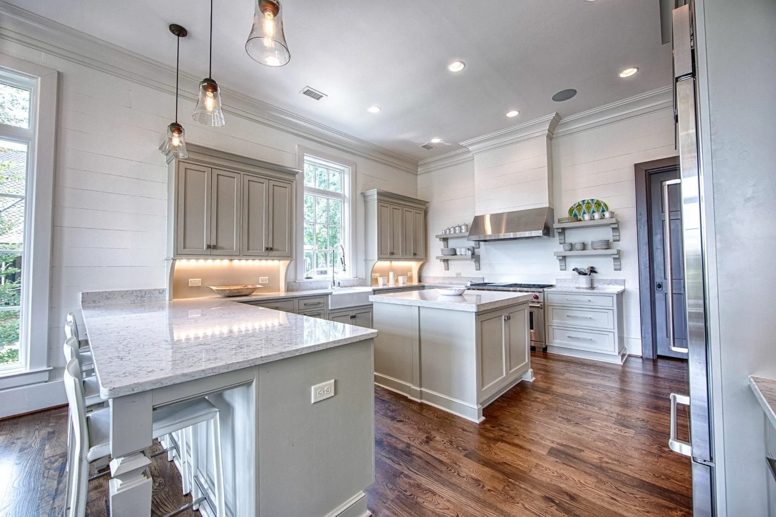 Bright custom kitchen with light gray cabinetry, white stone countertops, two islands, and warm wood flooring in an Alabama home.