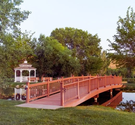 Outdoor wedding ceremony at The Shangri-La Event Center in Toquerville, Utah with pond, waterfalls, and gazebo backdrop. - Southern Utah Wedding Invitations
