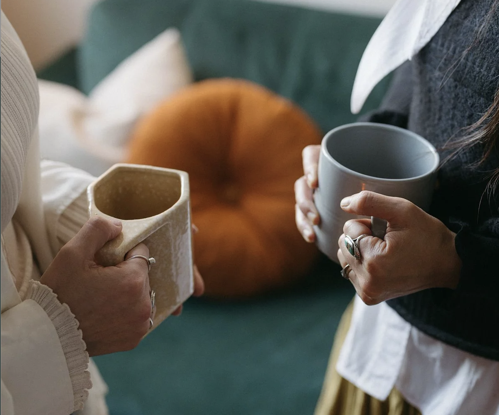 Dos personas sosteniendo tazas de cerámica, una color crema y la otra gris, en un entorno relajado con fondo difuso.