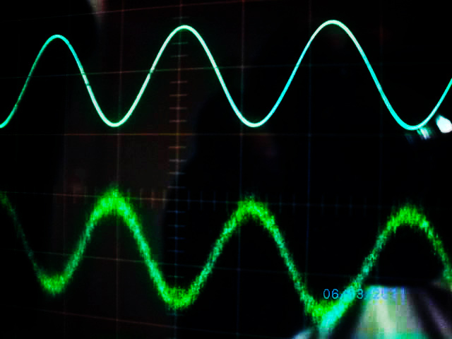 The top line is a smooth sine wave of alternating current (AC.) The bottom line is a sine wave corrupted with EMI.