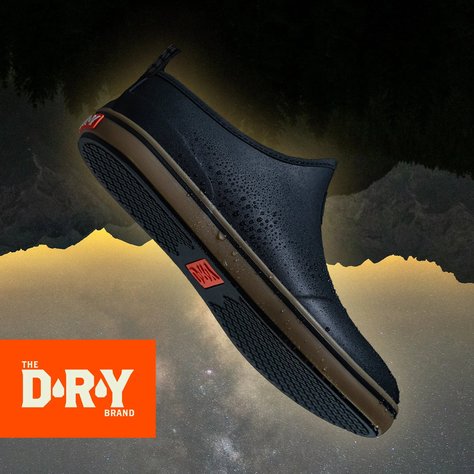 A black waterproof shoe with droplets of water on it lying against a starry night sky and mountain silhouette, with an orange logo reading 'The D-RY Brand' in the bottom left corner.