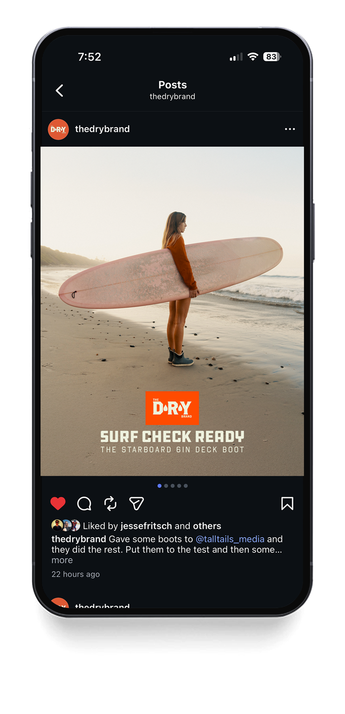 A woman standing on a beach holding a pink surfboard, looking towards the ocean at sunset.