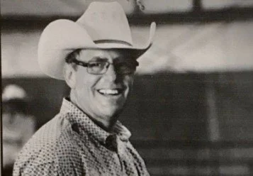 A man wearing a cowboy hat and glasses, smiling, in black and white.