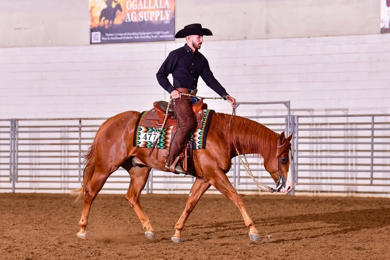 A man in western attire riding a chestnut horse inside an indoor arena.