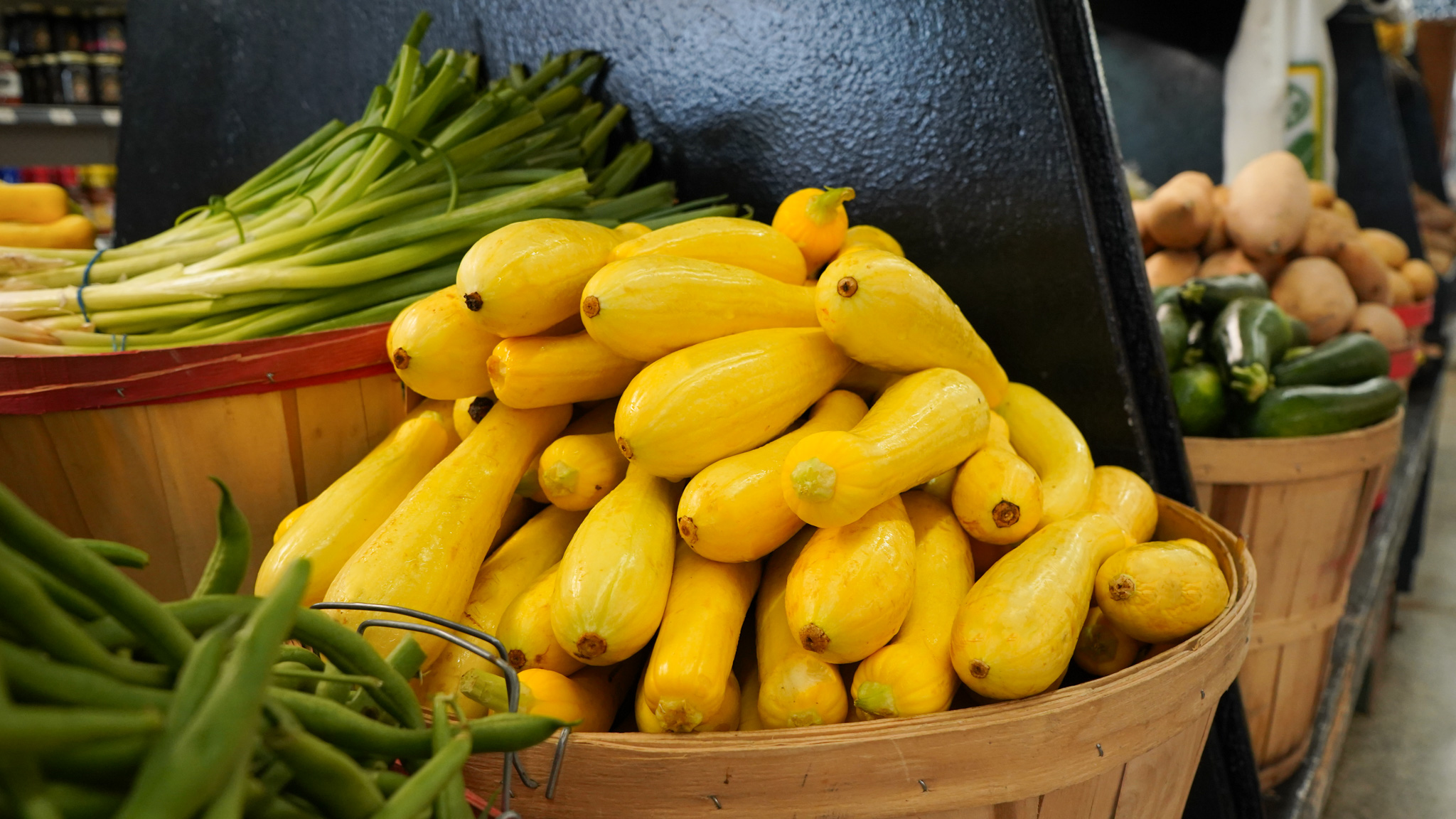 Produce section at a grocery store with lemons, limes, cucumbers, oranges, bananas, and various vegetables and packaged products.