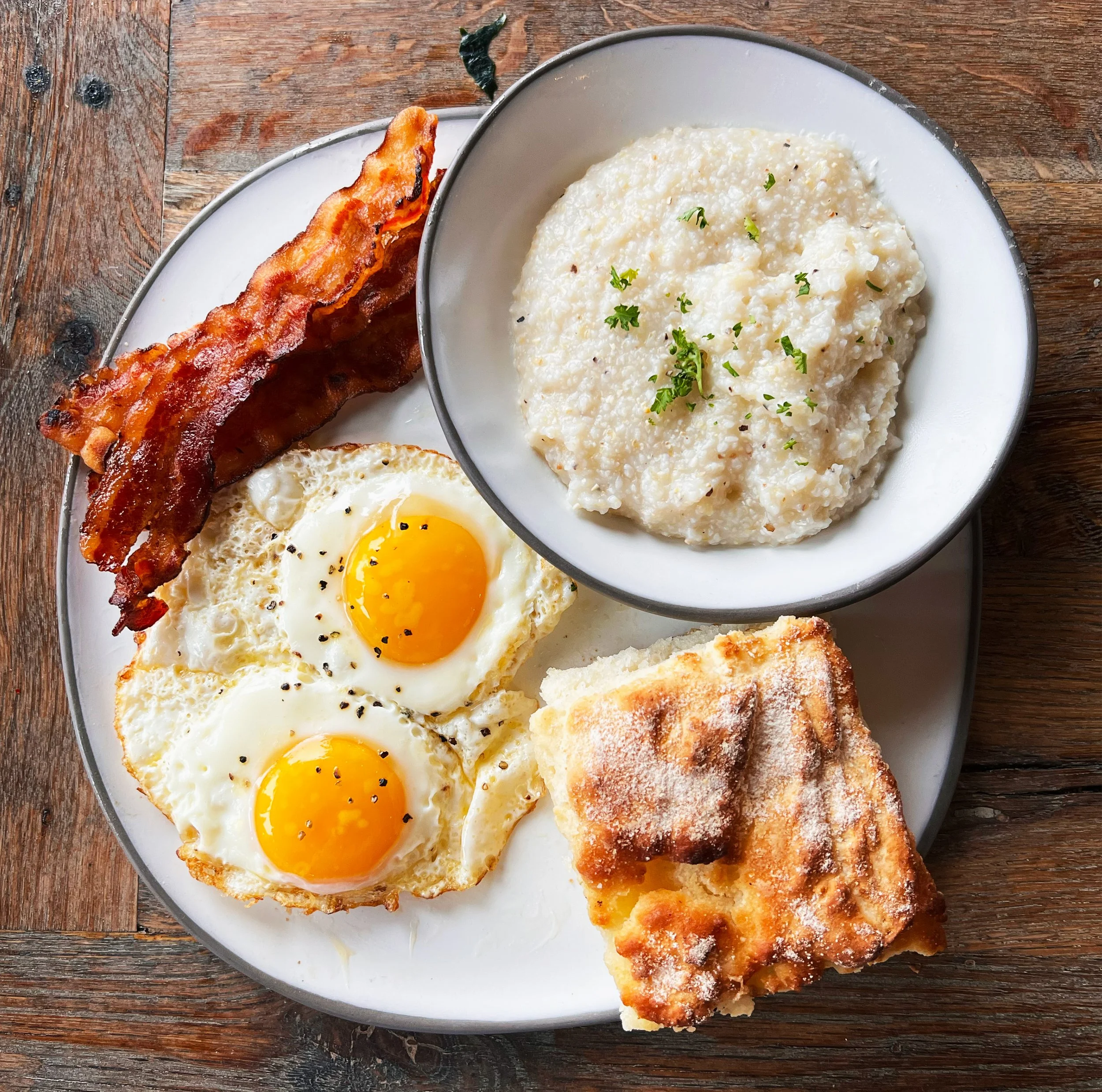 Brunch plate with eggs bacon grits and biscuit on a white plate