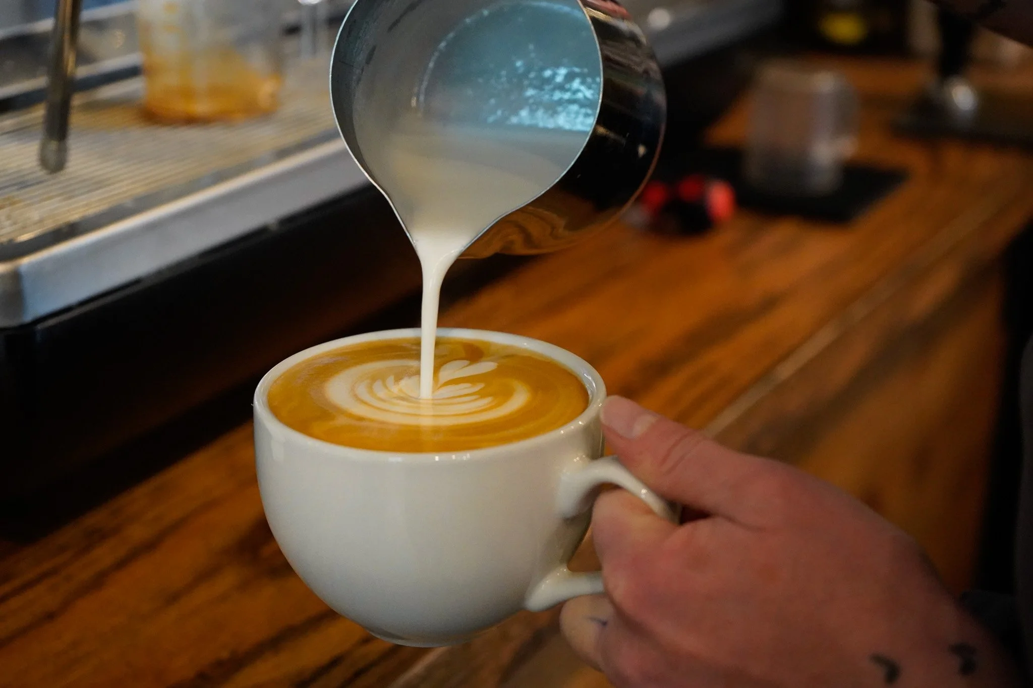 Coffee cup help in a hand with steamed milk being poured on top to create latte art