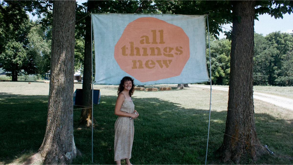 Lyric Morris-Latchaw in front of the banner she for All Thing New Festival.