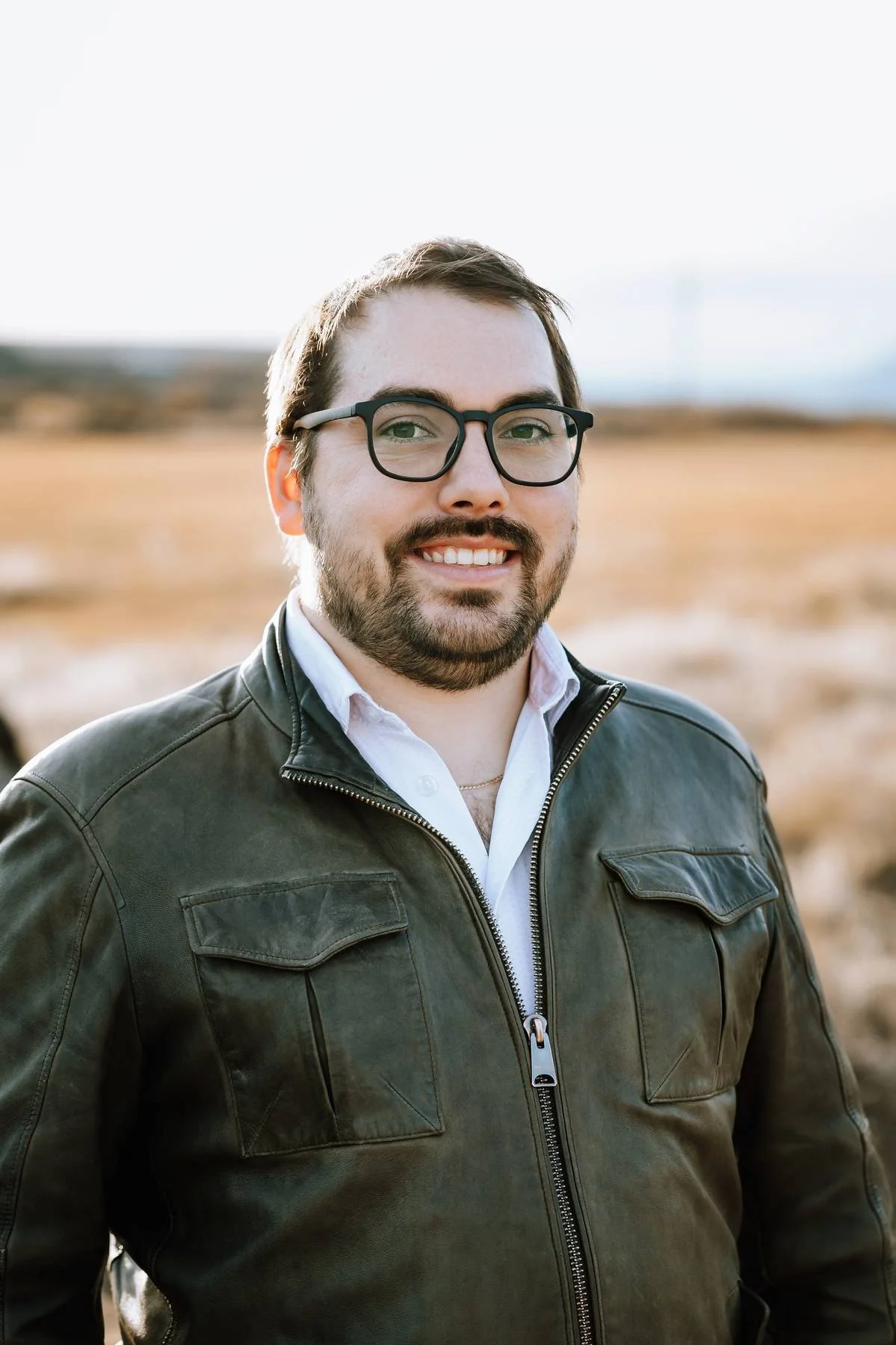 Man in leather jacket leaning against a wooden wall outdoors