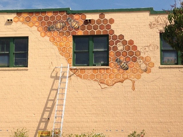 Ladder leaning against early version of mural with fewer honeycombs