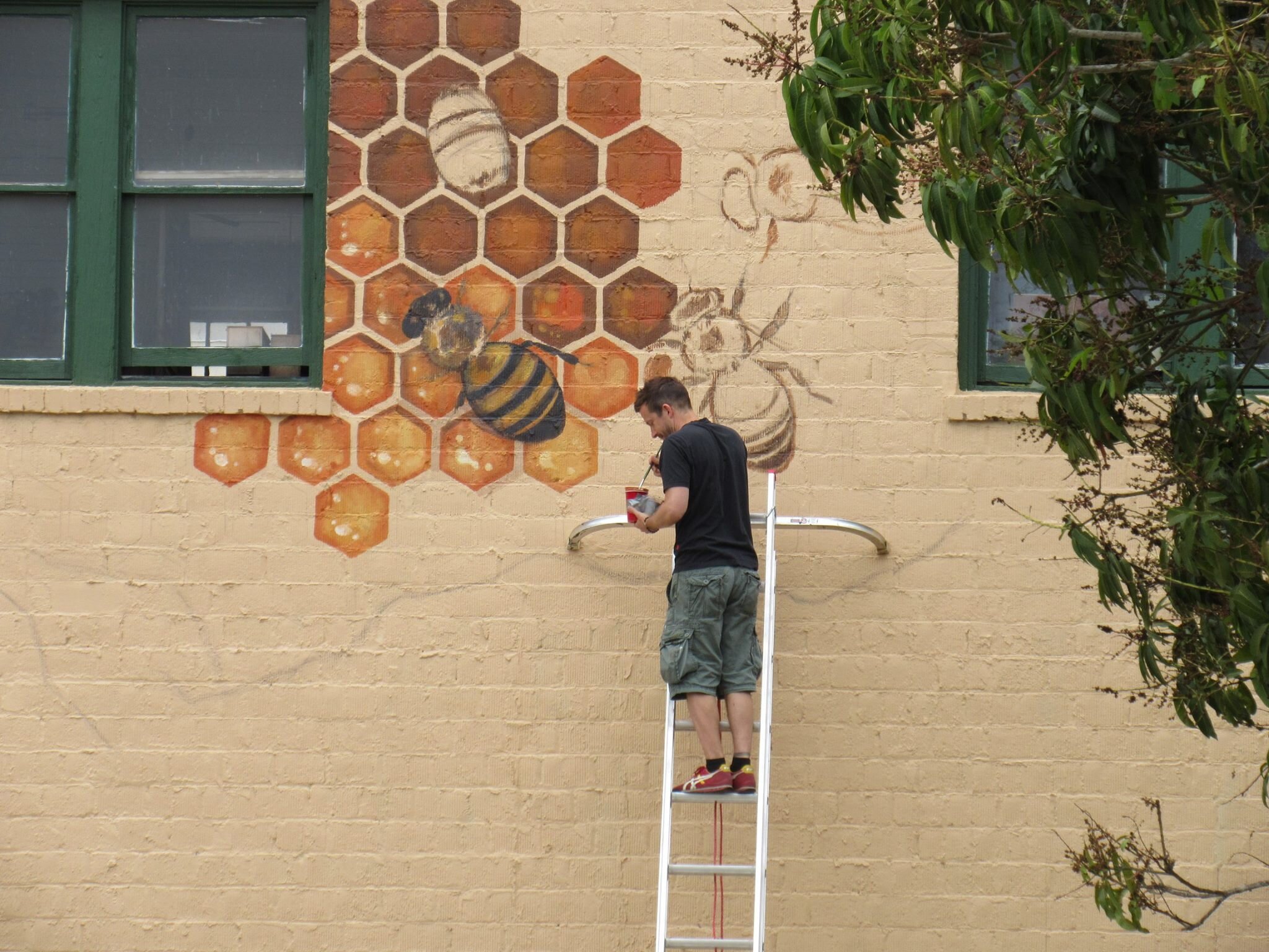 Matt Willey standing on a ladder painting a section of the mural