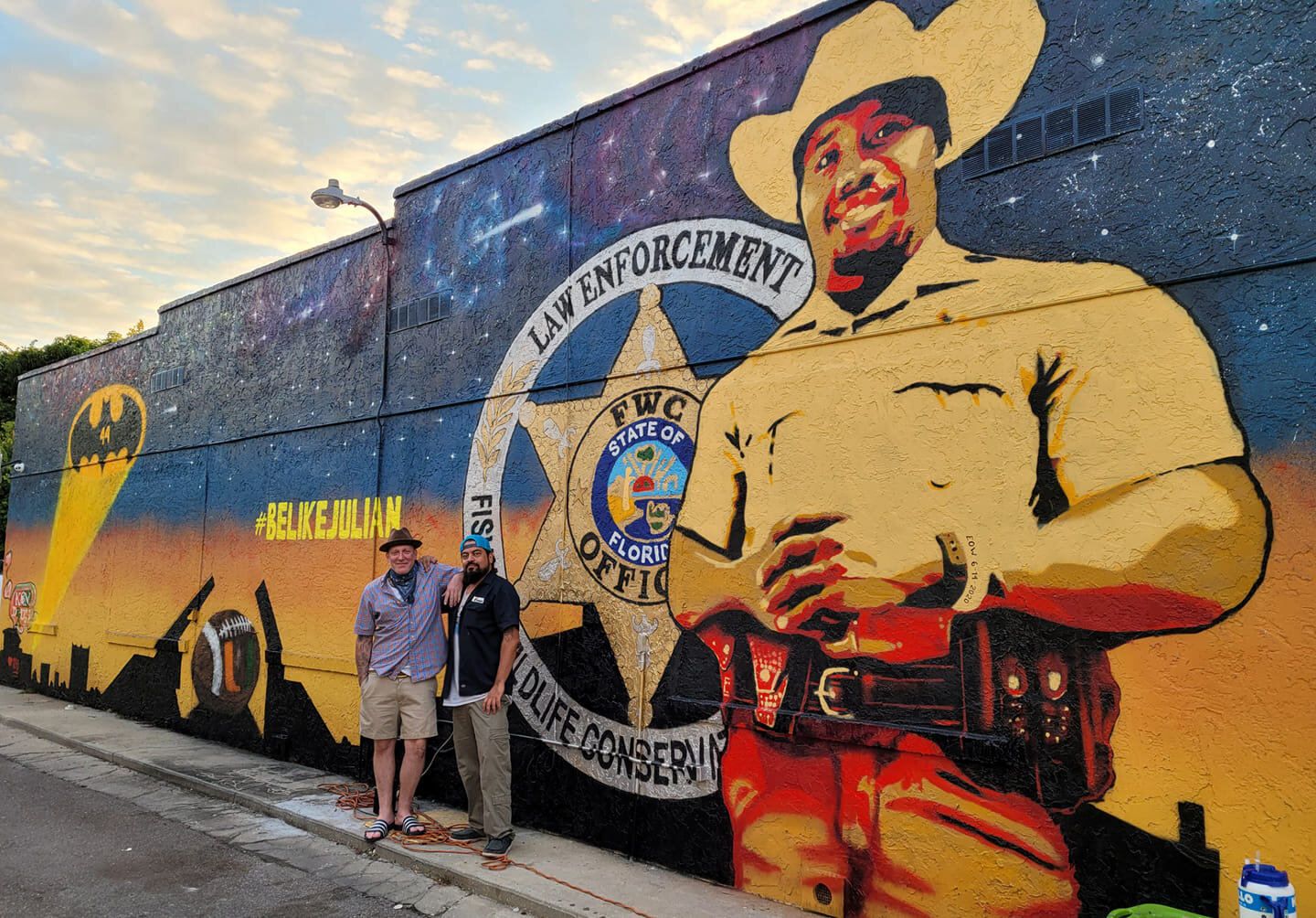 Two people pose for a photograph in front of the mural