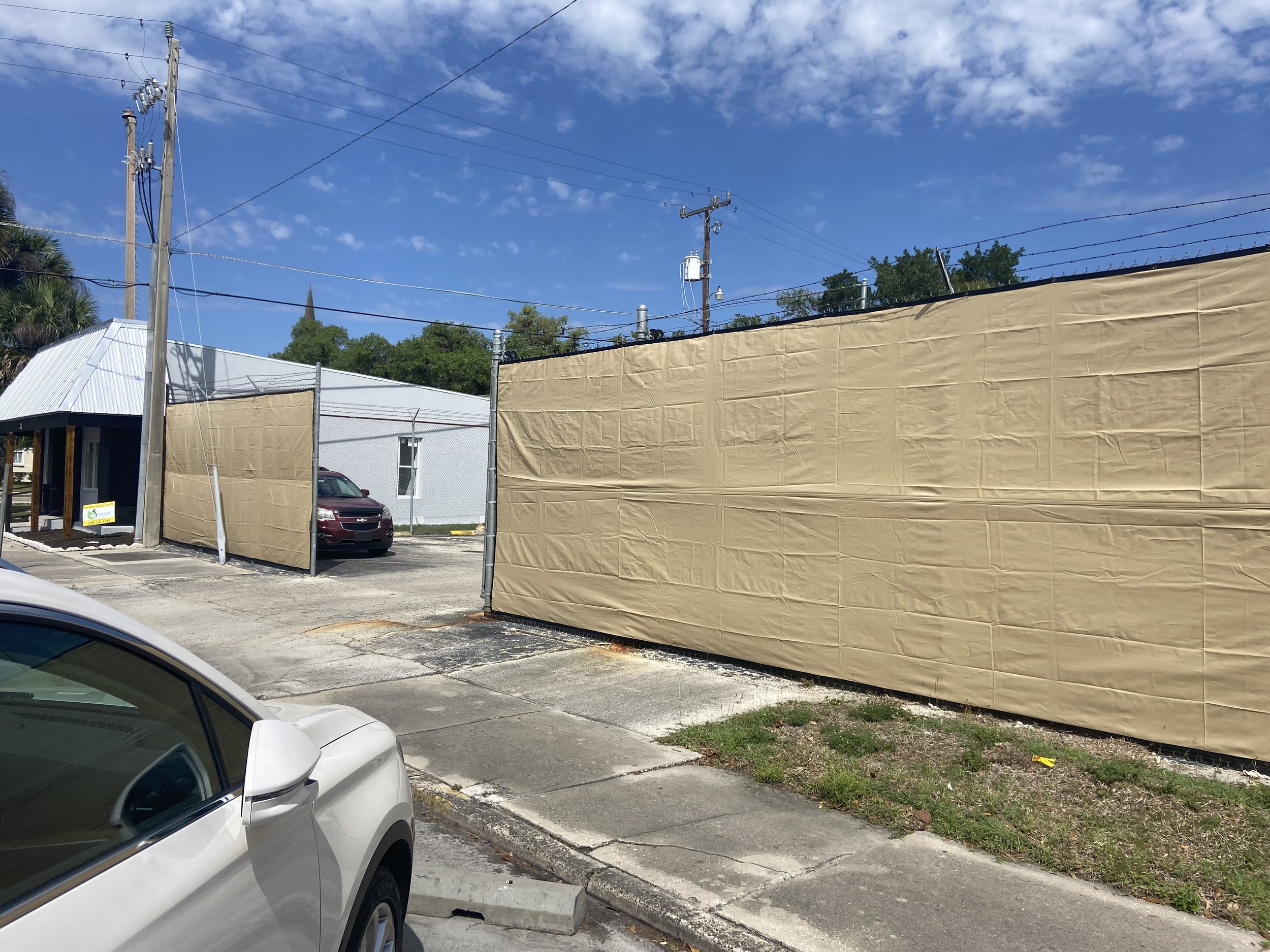 A beige fabric fence in the parking lot of the CenturyLink facility, blocking the industrial view from the street