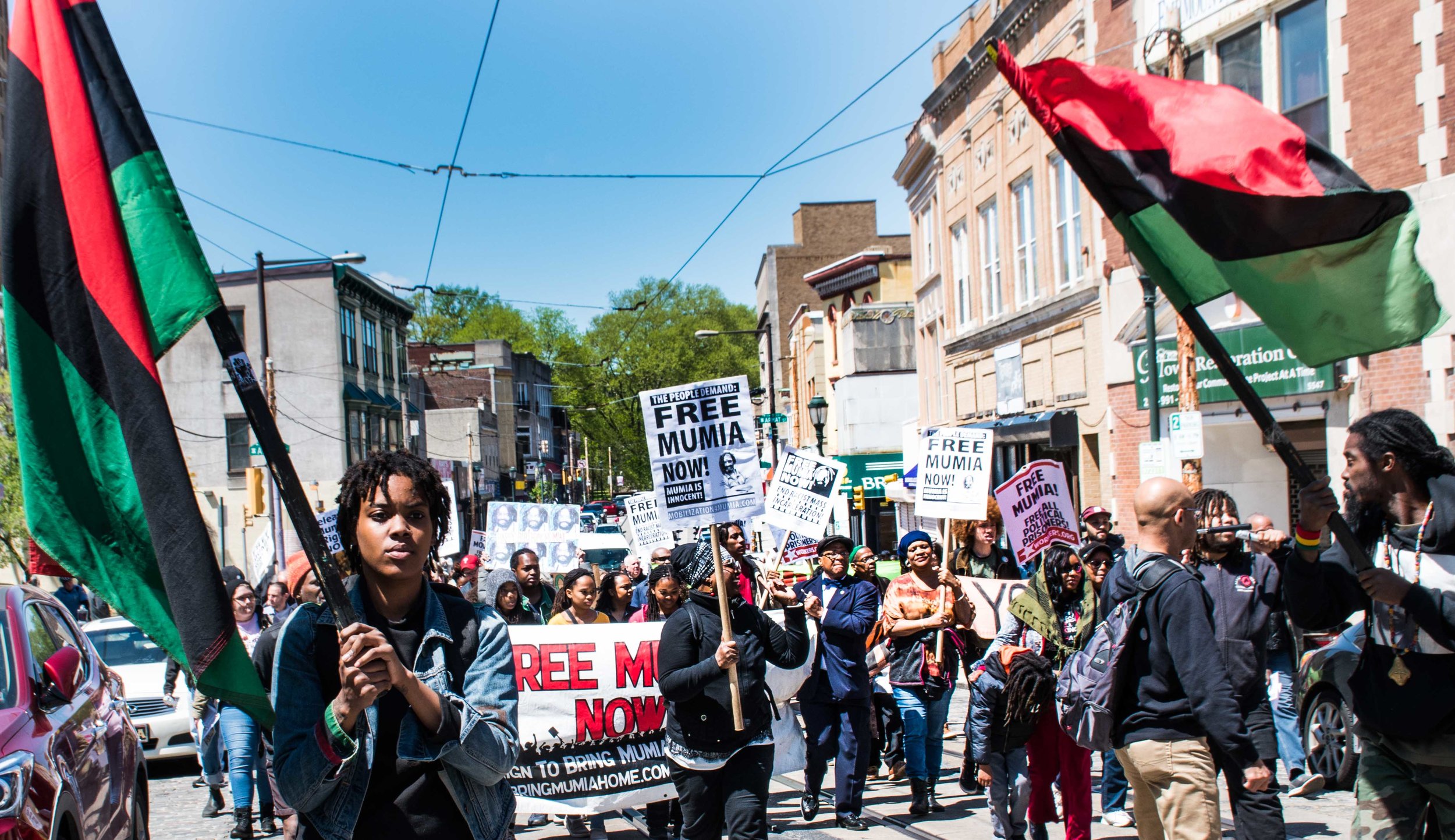 “Brick by Brick, wall by wall, we’re going to free Mumia Abu-Jamal” the chant on Germantown Ave April 27.  Photo credit - Joe Piette