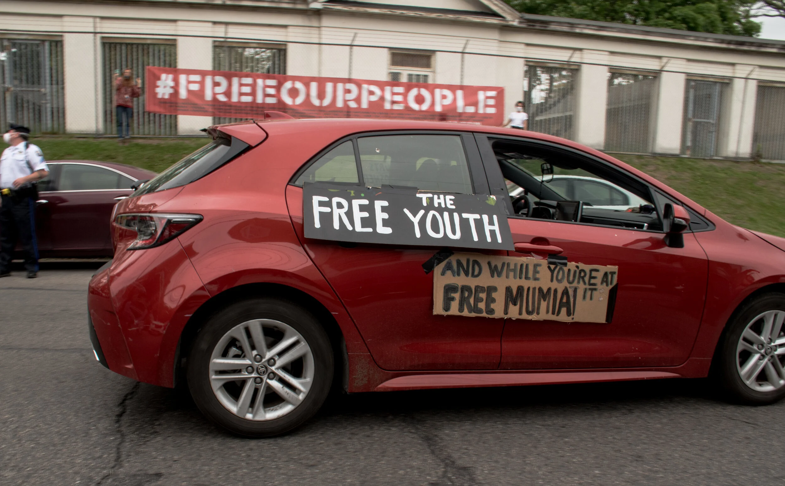 Philadelphia, May 18 - As states across the U.S. took steps to stop the spread of COVID-19 — closing schools and workplaces, canceling events and shifting to supporting children in their homes and communities — one group of young people is being left behind: the nearly 50,000 youth locked up across the country. Releasing young people held in detention centers was the focus of a “Free Our Youth” car caravan in front of the Philadelphia Juvenile Justice Services Center (PJJSC) on May 18. At least two children have tested positive for COVID-19 while in juvenile jail, but the number of incarcerated youth has actually increased from 105 on May 7 to 125 on May 18. Speaking outside the center’s front doors, formerly incarcerated young adults, families members of incarcerated young people, community leaders, City Council members and allies took turns describing the deep pain, fear, uncertainty and isolation that children have experienced while locked behind bars, separated from their families during the worst public health pandemic in a century. Photo shows one of the caravan vehicles with a FREE MUMIA sign. More details at  https://www.workers.org/2020/05/48851/  .