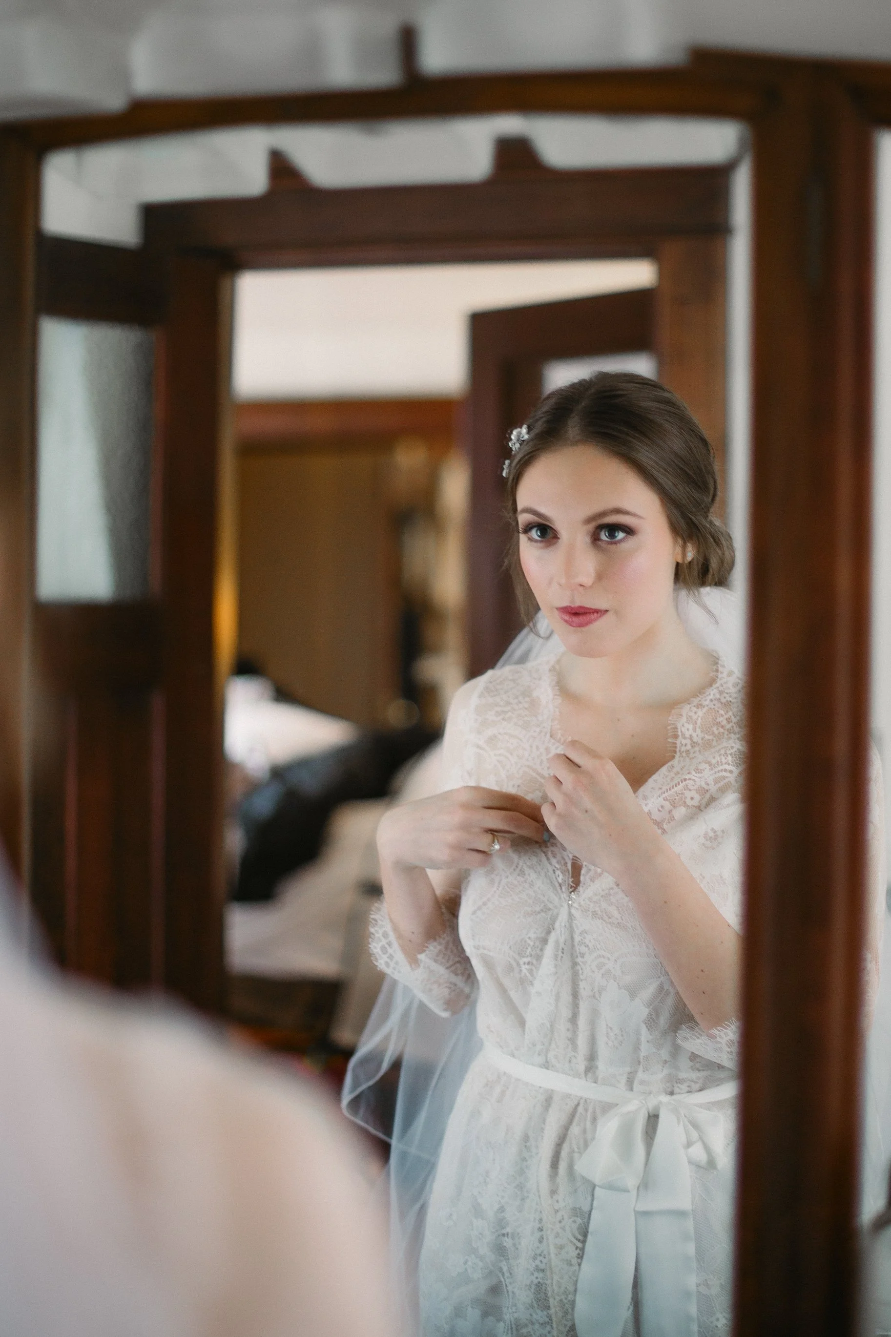 A young woman in a lace wedding dress looking at herself in a mirror, adjusting her dress.
