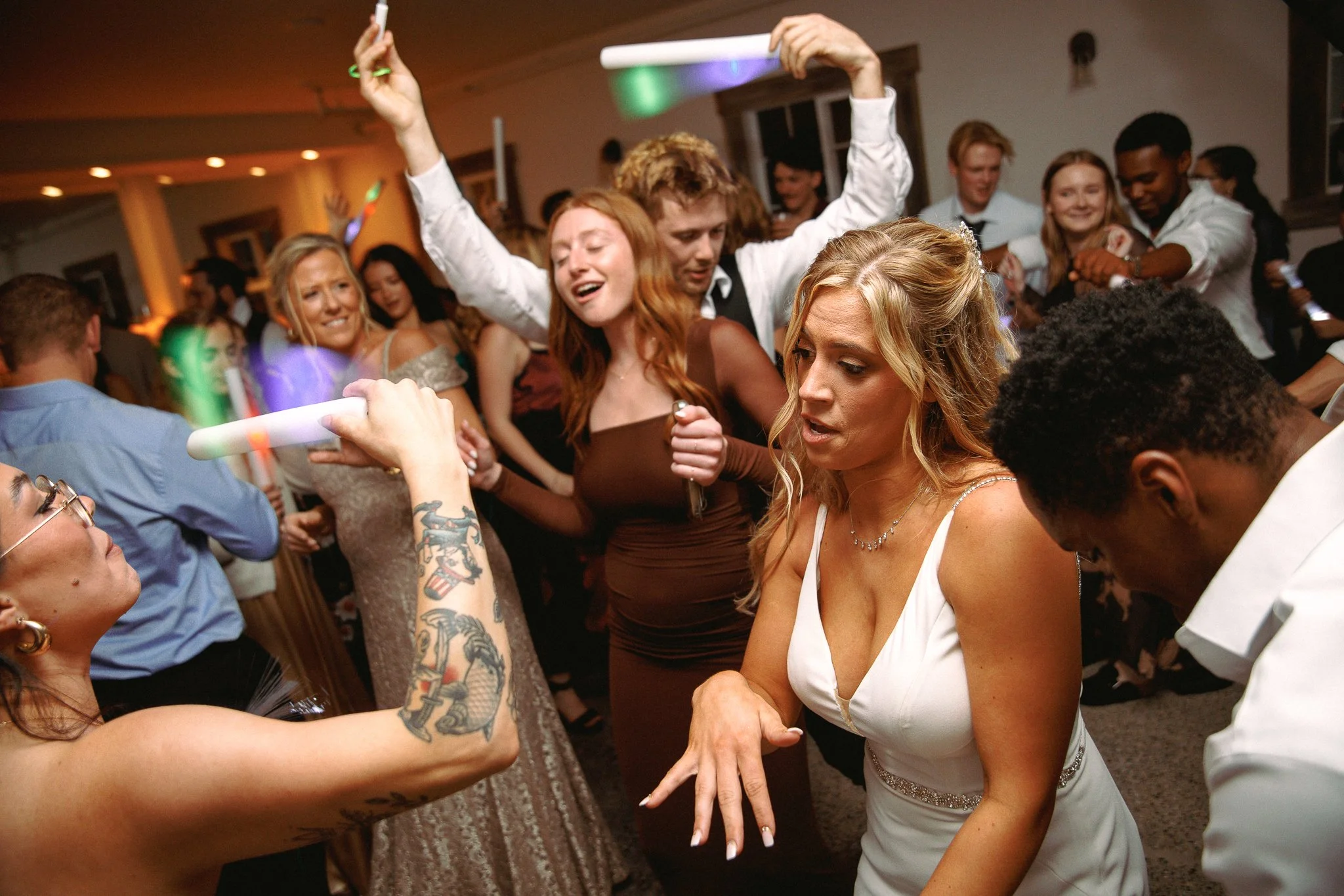 People dancing and celebrating at a wedding reception, with colorful lights and a lively atmosphere.