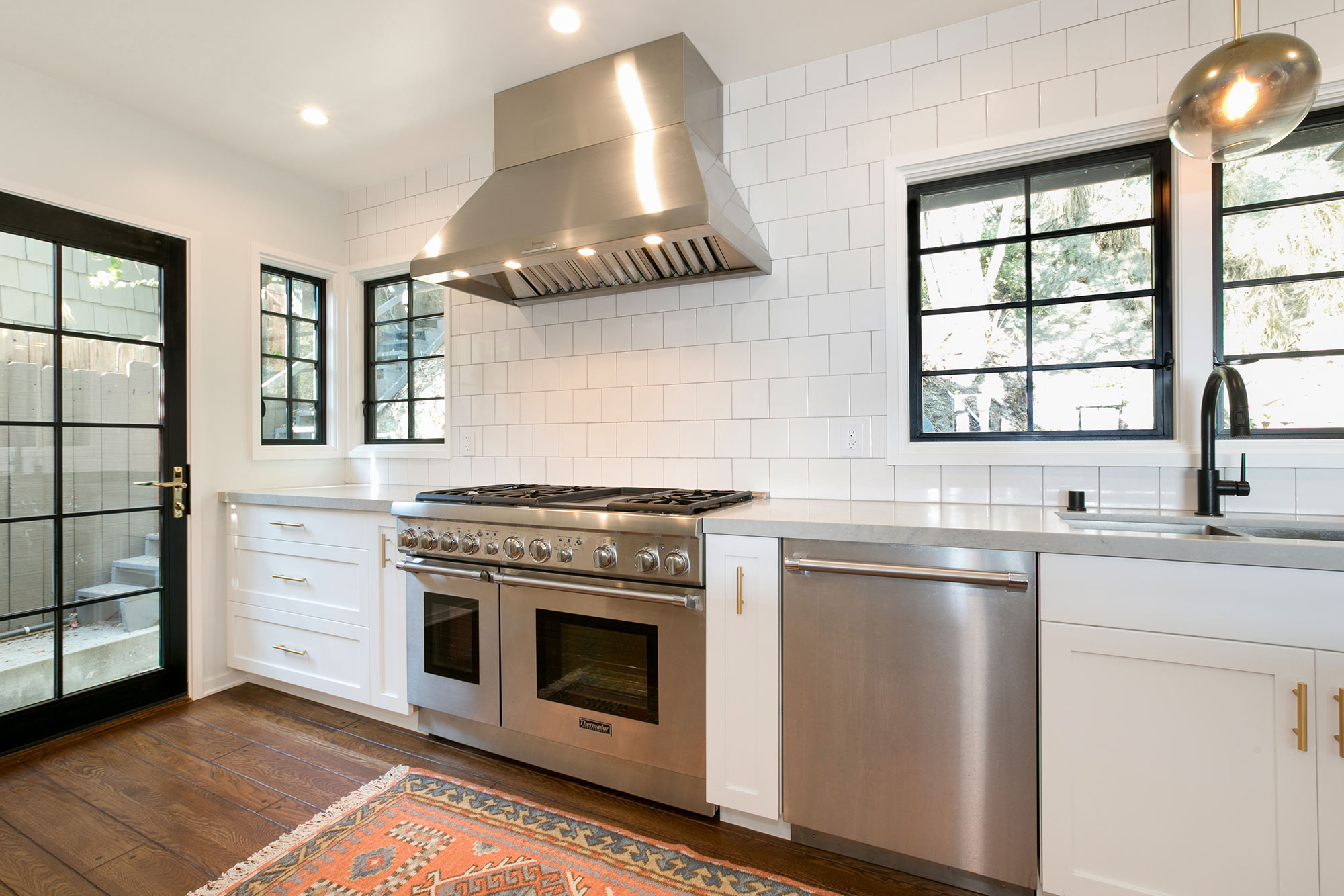  The new open kitchen features custom-made white shaker cabinets with gold pulls and knobs, black fixtures, new hardwood floors, white 5"X5" ceramic tile backsplash, Caesarstone Noble Grey countertops, breakfast bar with pattern cement tile detail, T