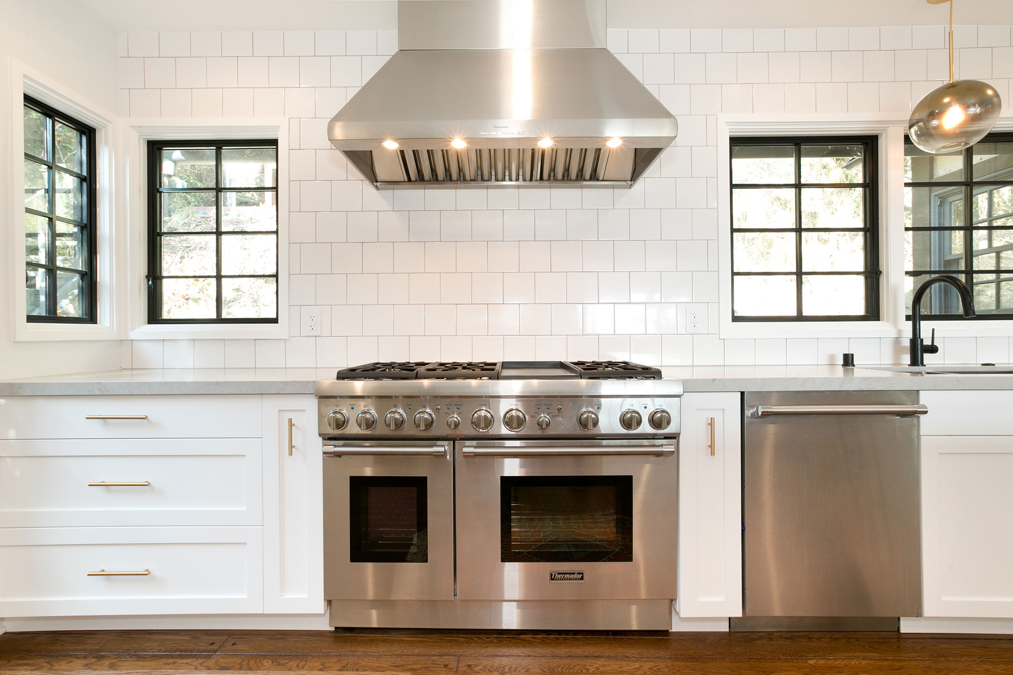  The new open kitchen features custom-made white shaker cabinets with gold pulls and knobs, black fixtures, new hardwood floors, white 5"X5" ceramic tile backsplash, Caesarstone Noble Grey countertops, breakfast bar with pattern cement tile detail, T