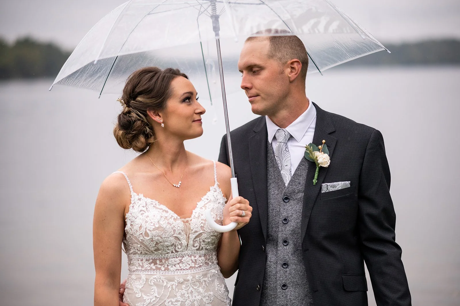 Bride and Groom look at each other while standing under a clear umbrella Twin Birch Studio
