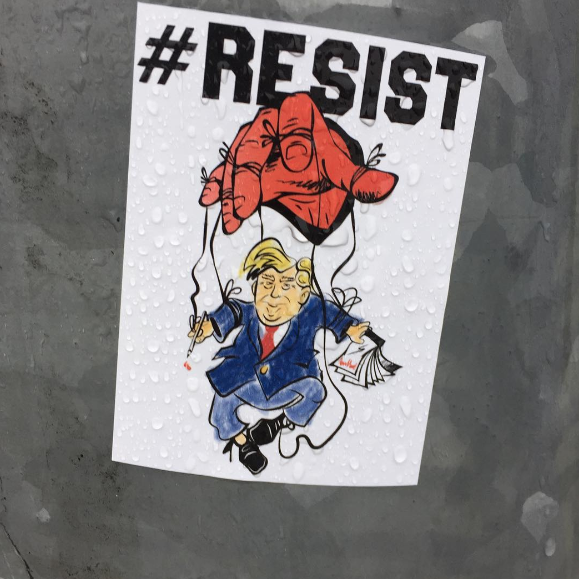 Picture of President Trump as a marionette doll controlled by a red hand with the caption "#RESIST"