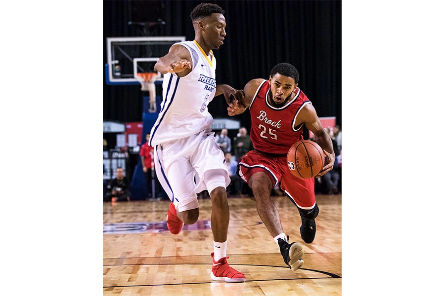 Brock University’s Tyler Brown (#25) drives to the basket despite strong defence from Ryerson University’s Jean-Victor Mukama (#8).
