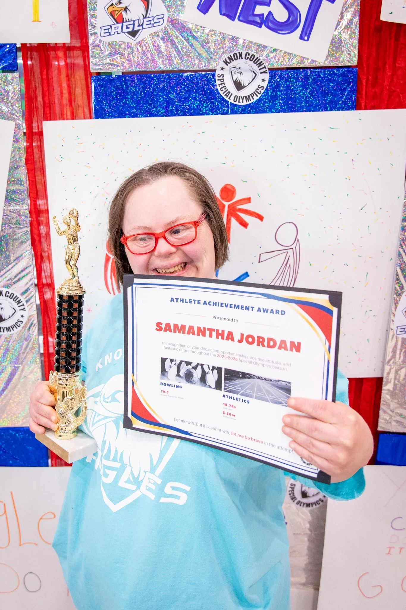 portrait of a person standing in front of a special olympics back drop, holding their trophy and certificate
