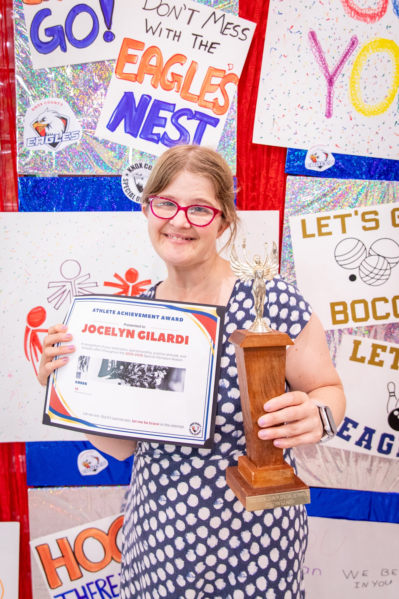 portrait of a person standing in front of a special olympics back drop, holding their trophy and certificate