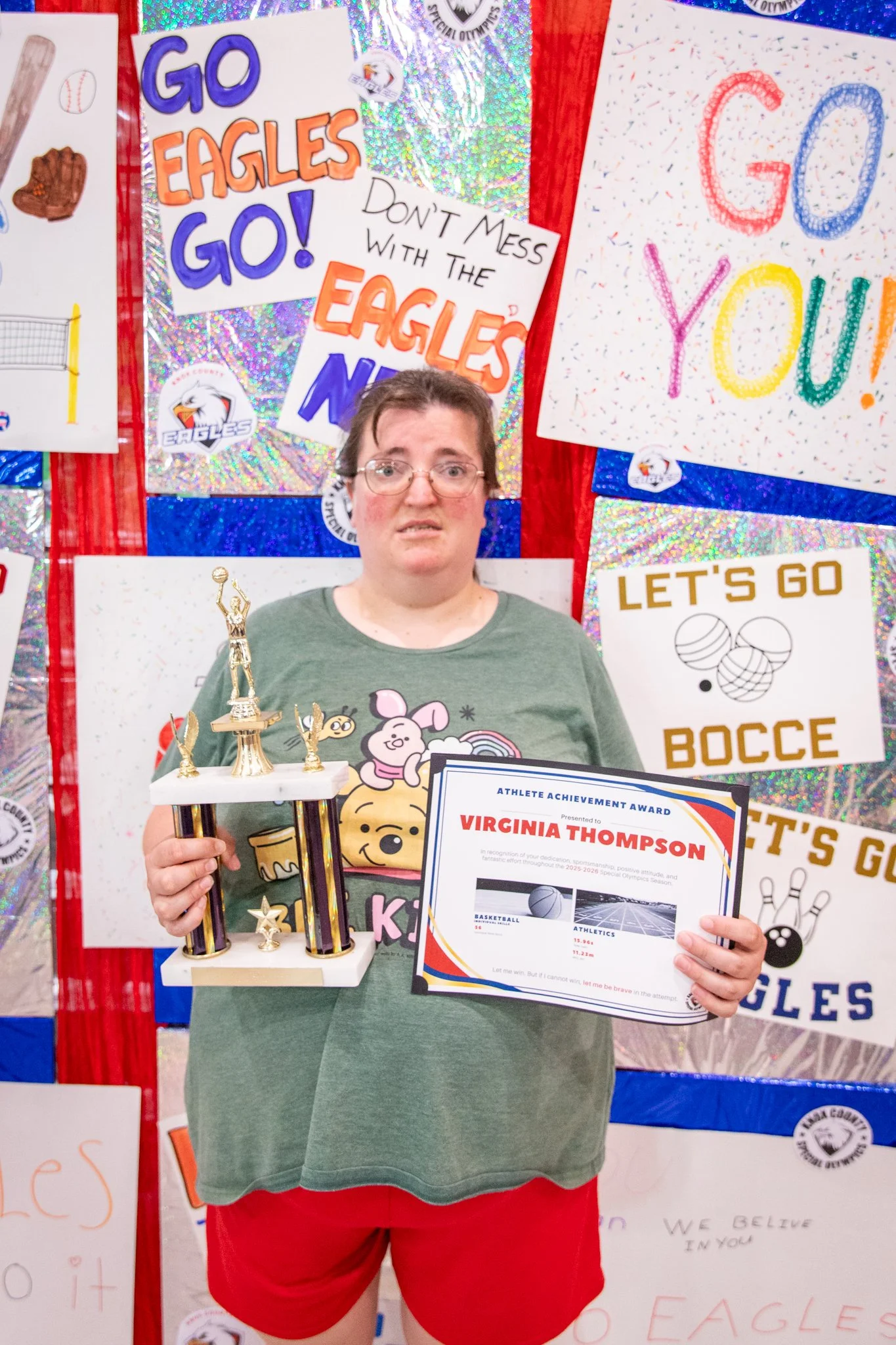 portrait of a person standing in front of a special olympics back drop, holding their trophy and certificate