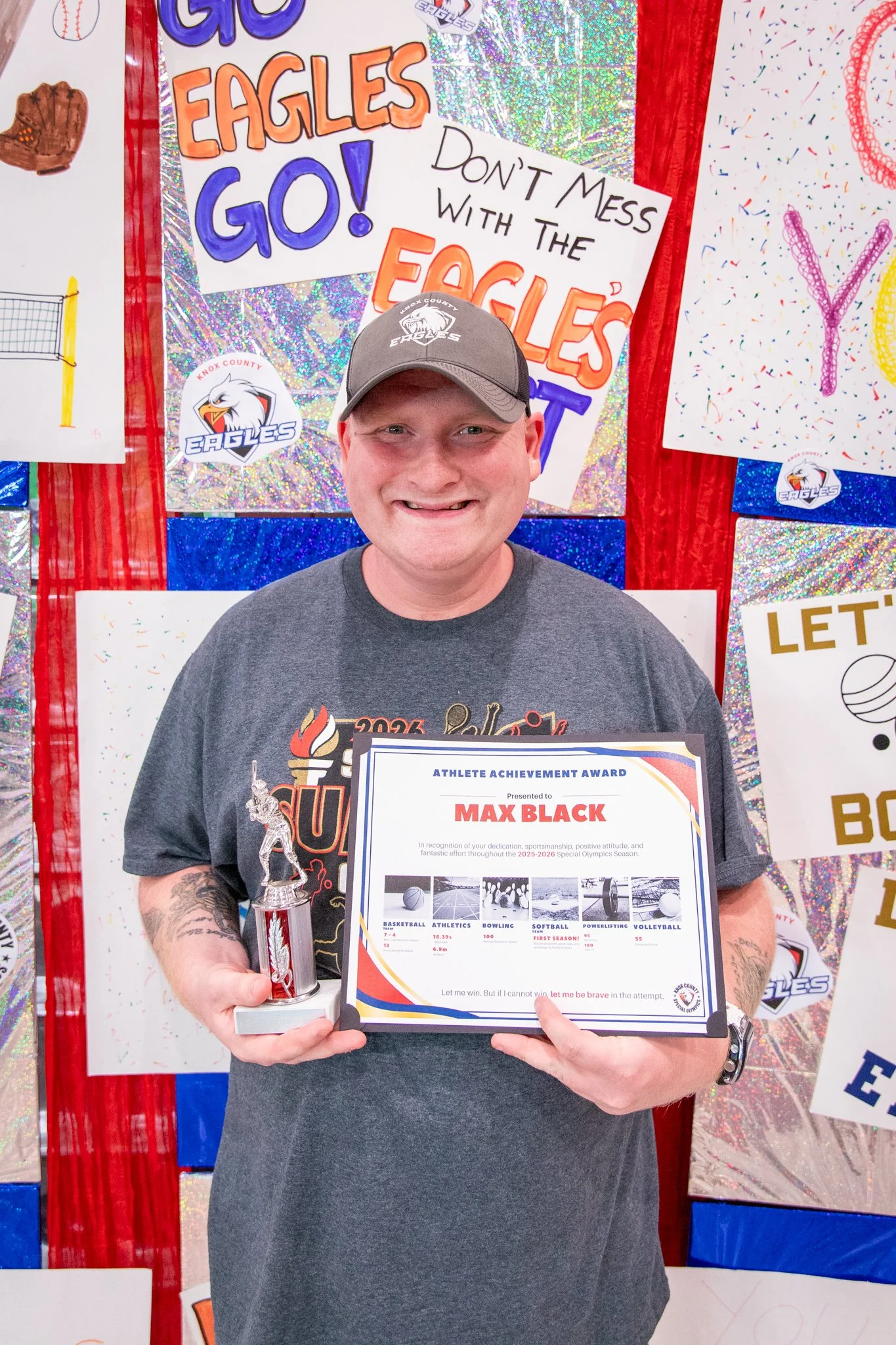 portrait of a person standing in front of a special olympics back drop, holding their trophy and certificate