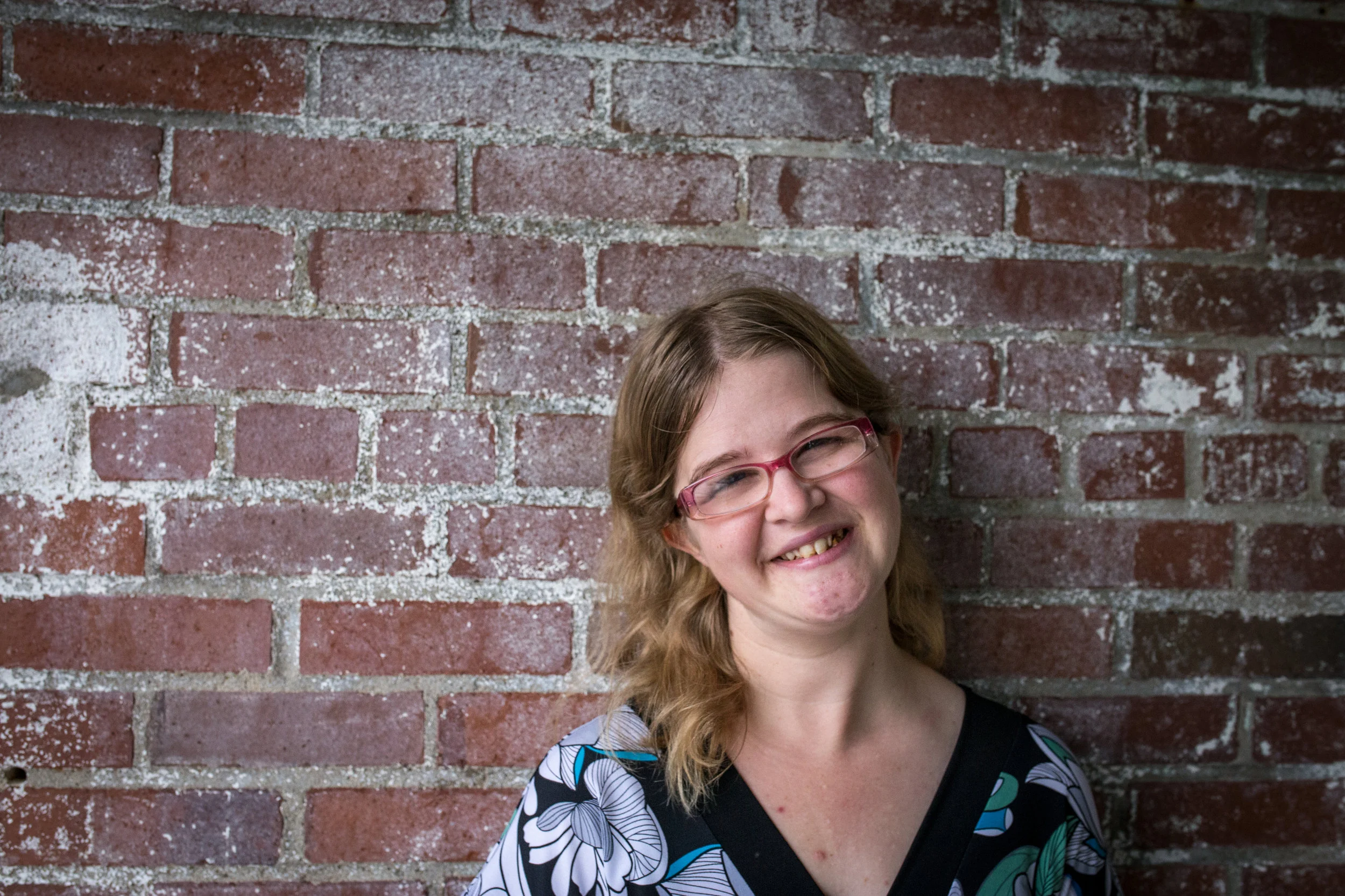portrait of young woman with disability smiling, standing in front of brick wall